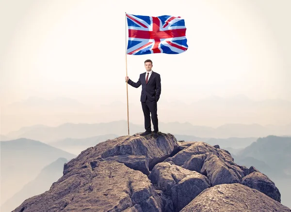 Zakenman op de top van een rots vlag houden — Stockfoto