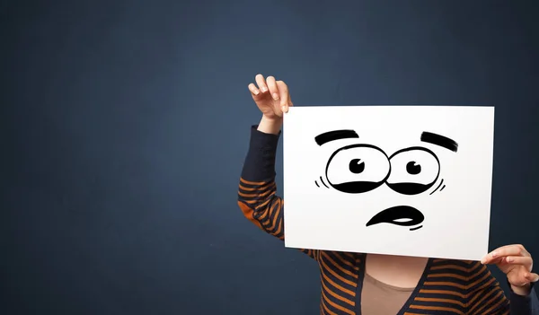 Person holding a paper with funny emoticon in front of her face — Stock Photo, Image