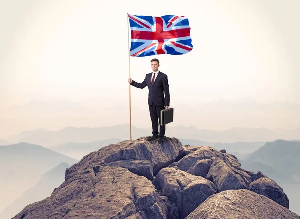Businessman on the top of a rock holding flag