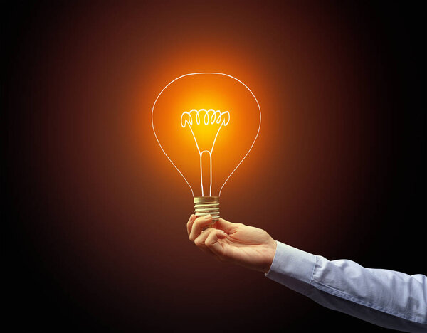 рука держа лампочку на темном фоне