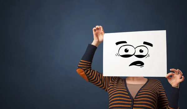 Person holding a paper with funny emoticon in front of her face — Stock Photo, Image