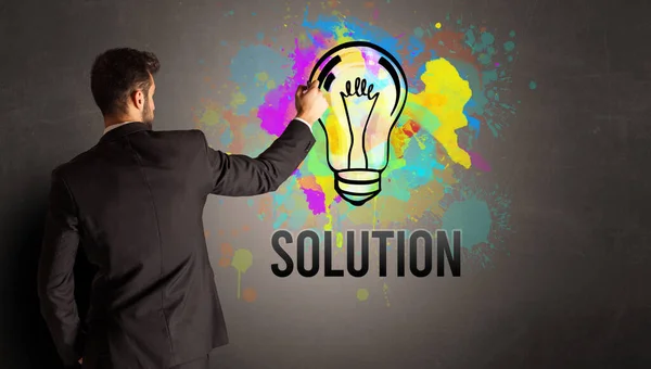 Businessman drawing colorful light bulb — Stock Photo, Image