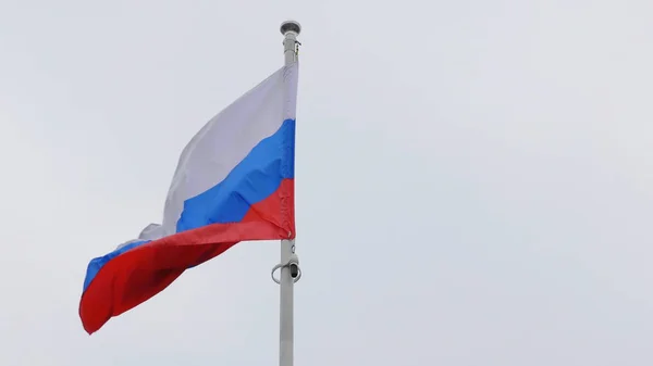 Bandeira russa no mastro acenando ao vento contra um céu azul com nuvens — Fotografia de Stock