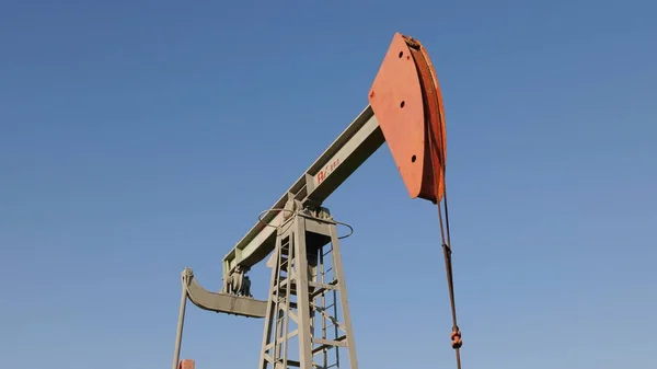 Эксплуатация нефтегазовой скважины на нефтяном месторождении, профилированной на фоне голубого неба — стоковое фото