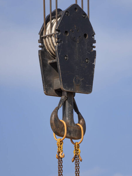 Crane hook with red and white stripes hanging, blue sky in background
