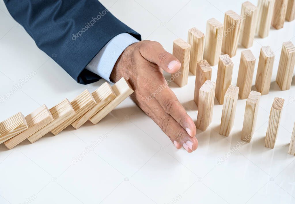 Close up of businessmans hand stopping the domino effect on the wooden blocks with copy space