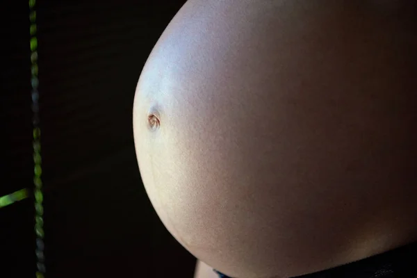 Brzuch kobiety w ciąży w oświetleniu bocznym. Zbliżenie. — Zdjęcie stockowe
