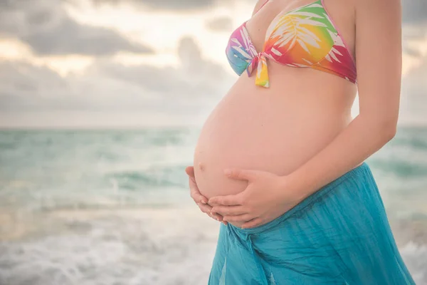 Manos madres y padres en el abdomen de una embarazada. Un vestido verde . —  Fotos de Stock