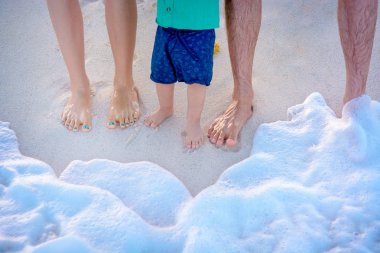 Legs of the father, mother and son on the sand on the beach clipart