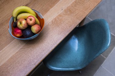 Tahta bir masada meyve kasesi ve mavi bir cam sandalye.