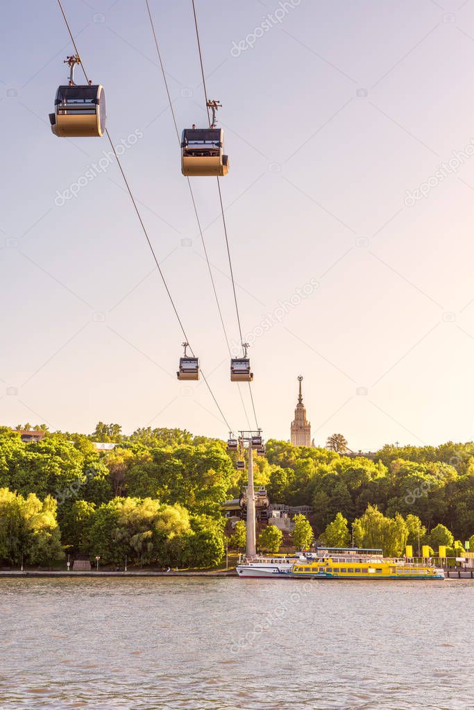 Scenic view of the cable car between Sparrow Hills and Luzhniki Stadium in Moscow, Russia. Cableway cabins hang in the sky above Moskva River in Moscow. Main building of Moscow University in distance.