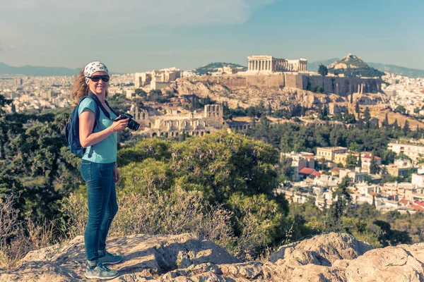 かわいい若い女性は アテネ ギリシャの丘の上からアクロポリスの写真を撮る 有名な古代ギリシャのアクロポリスはアテネの主要なランドマークです アテネとカメラで笑顔の女性観光客を訪問します — ストック写真