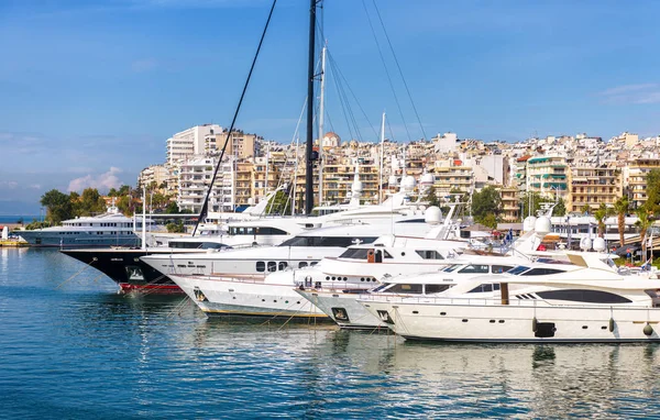 Yachts docked in sea port in Piraeus, Athens, Greece. Modern motor boats mooring in beautiful marina in summer. Scenic view of white yachts in harbor. Concept of luxury marine relax and vacation.