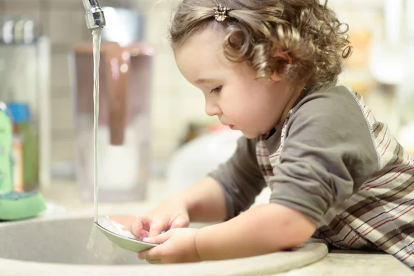 Malé dítě myje nádobí v kuchyni — Stock fotografie