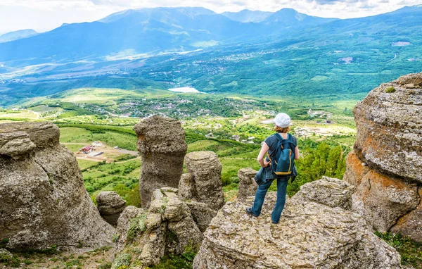 Landscape of Crimea. Young woman on bizarre stones of the Valley of Ghosts. This place is a tourist attraction of Crimea. Panoramic view of South Crimea mountains. Travel and hiking concept.