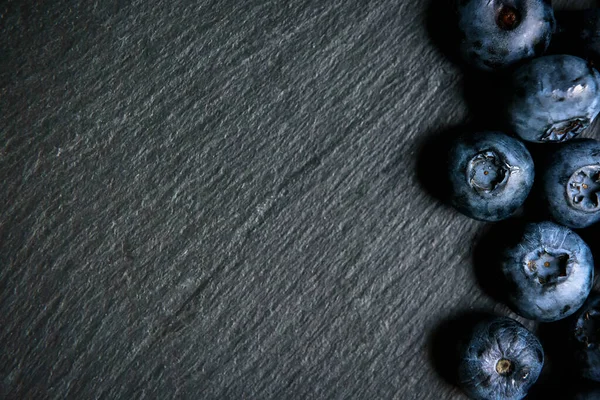 Blueberry berries on slate texture background, fresh blueberry or bilberry with copy space. Top view of dark table background and blueberry, flat lay. Concept of fruit nutrition and organic food.