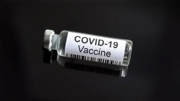 COVID-19 coronavirus vaccine on black desk, medication with vaccine for corona virus cure in lab. Close-up small vaccine bottle. Concept of medicine, trial and treatment due to SARS-CoV-2 coronavirus.