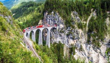 Landscape with Landwasser Viaduct in summer, Filisur, Switzerland. It is landmark of Swiss Alps. Panoramic view of railroad bridge and red train. Rhaetian glacier express runs on amazing railway. clipart