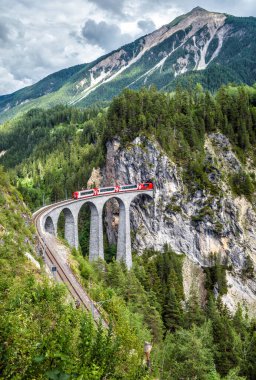 Yazın Landwasser Viaduct, Filisur, İsviçre. İsviçre Alpleri 'nin simgesidir. Demiryolu köprüsü ve kırmızı trenin manzarası. Rhaetian ekspresi ile dağlık bölgede dağ yolunda uzanan bir arazi..