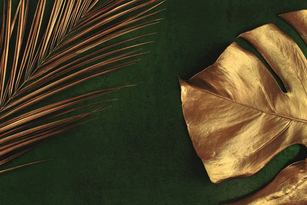 Gouden Palm en Monstera bladeren op donker groene achtergrond — Stockfoto