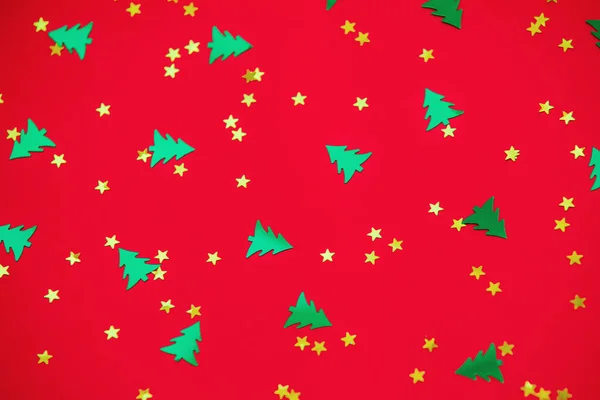 Green christmas trees and gold stars confetti sparse on red back — Stock Photo, Image