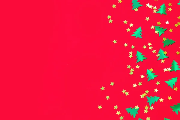 Green christmas trees and gold stars confetti sparse on red back — Stock Photo, Image