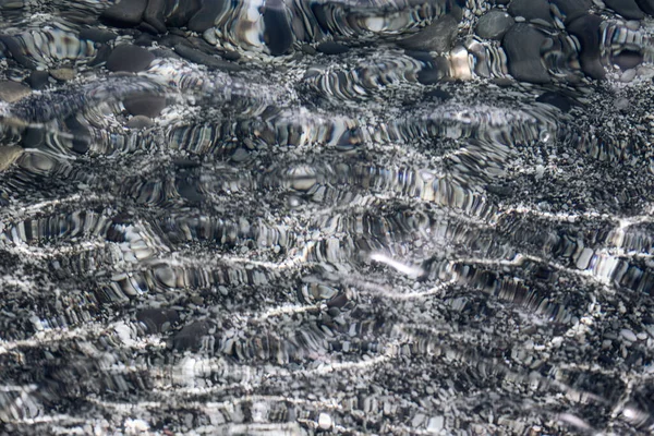 Superficie transparente de agua clara y tranquila con pequeñas piedras grises textura del fondo del mar —  Fotos de Stock