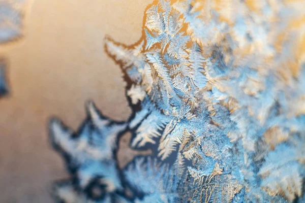 The texture of the frosty patterns. Winter frosty blue patterns on glass pink background