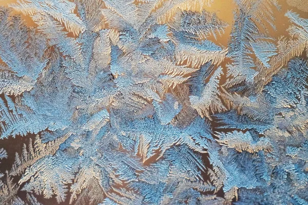 The texture of the frosty patterns. Winter frosty blue patterns on glass pink background