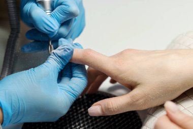 Elektrikli cihaz makine kullanarak donanım manikür. tırnak cilası uygulamadan önce çivi hazırlanması için yordam. Elinde manikürcü mavi eldiven ve istemci çivi. Kadın Güzellik Salonu. 