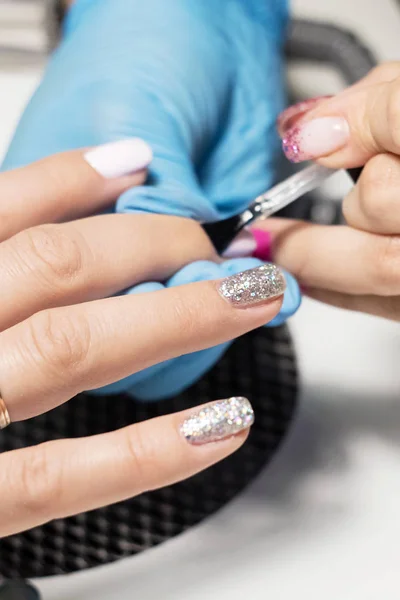 Hardware Manicure using electric device machine. procedure for the preparation of nails before applying nail polish. Hands of Manicurist in blue gloves and Nails of Client. Woman In Beauty Salon.