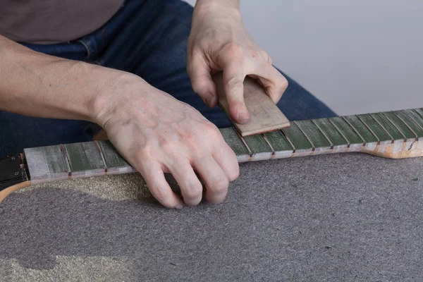 the master polishes the frets on the fretboard of the guitar. The fingerboard is protected by molar tape