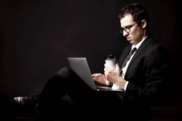 Brutal guy in a black suit with coffee. Black background. Coffee with you.  Manager.