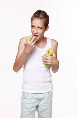 Beyaz gömlekli genç bir adam, bir elinde iki elma tutuyor ve diğer eliyle gömleğe bir elma siliyor. Stüdyoda beyaz bir arka planda. Duygular, meyve, yaşam tarzı, mutlu çocukluk..