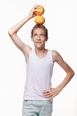 Beyaz gömlekli genç bir adam oynuyor, kafasında iki portakal var. Stüdyoda beyaz bir arka planda. Duygular, meyve, yaşam tarzı, mutlu çocukluk..
