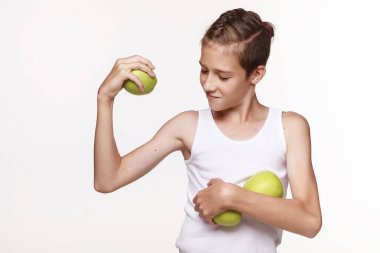 Beyaz gömlekli genç bir adam, elinde bir elma tutuyor ve pazılarını gösteriyor. Stüdyoda beyaz bir arka planda. Duygular, meyve, yaşam tarzı, mutlu çocukluk..