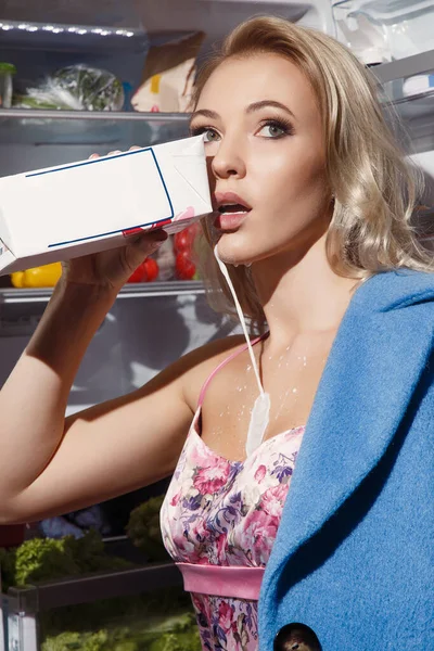 Vacker flicka dricker mjölk nära kylskåpet — Stockfoto