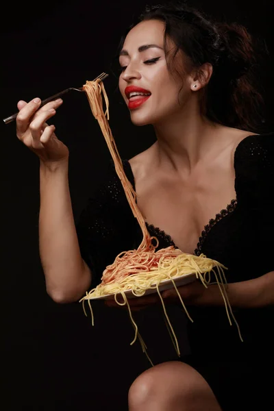 En vacker flicka äter med en gaffel spaghetti med röda läppar. — Stockfoto