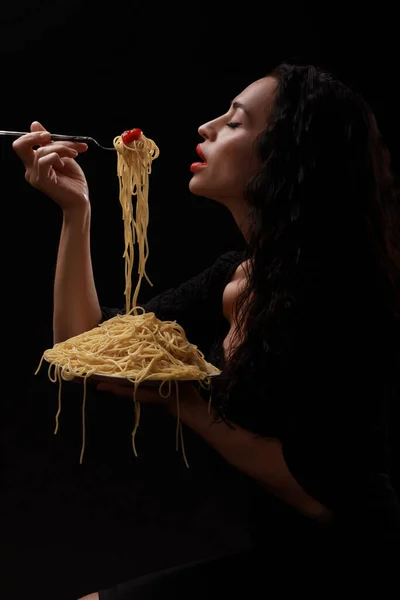 En vacker flicka äter med en gaffel spaghetti med röda läppar. — Stockfoto