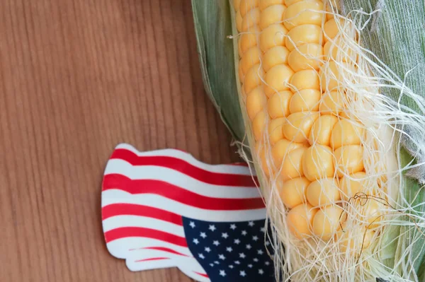 Geleneksel öğle yemeği konsepti, kartpostal. Uygun durum kartı şablonu için arkaplan veya kopya alanı ile kaplan. Fotokopi alanı olan taze mısırın yakın çekim detayları. Tahta zeminde kürdanla kağıttan yapılmış küçük bir Amerikan bayrağı.