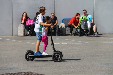 Parma, İtalya - 17 Eylül 2016: çocuk bir elektrikli scooter ve şehir merkezinde bankların üzerinde oturan insanlar sürme