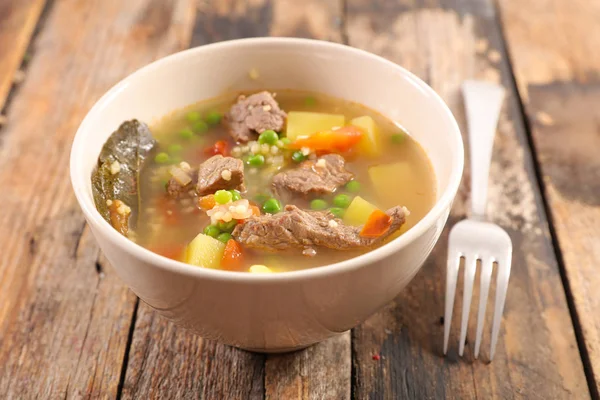 Beef soup with vegetables in white bowl and fork