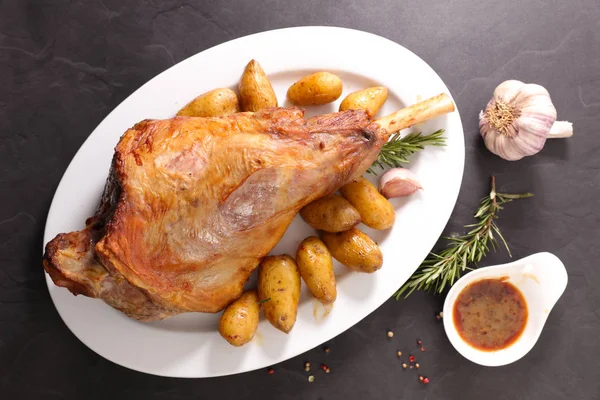 Baked lamb leg and potatoes on white long plate