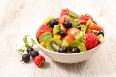 Ahşap masa üzerinde beyaz kase taze meyve salatası