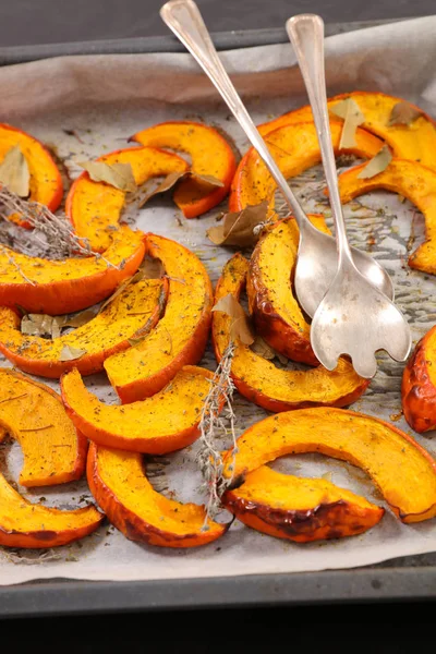 Grilled pumpkin slices with kitchen spoons on tin