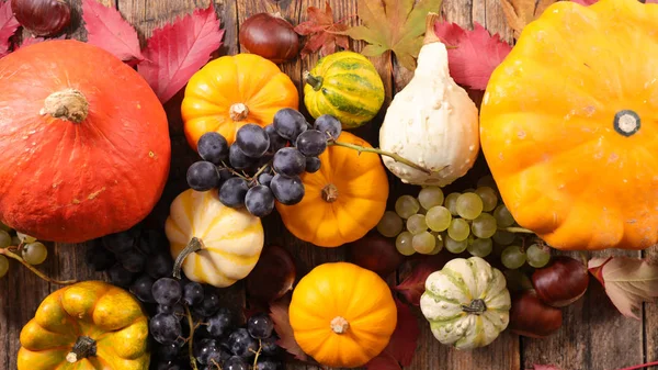 different sort of pumpkins with leaf and grapes on wood background