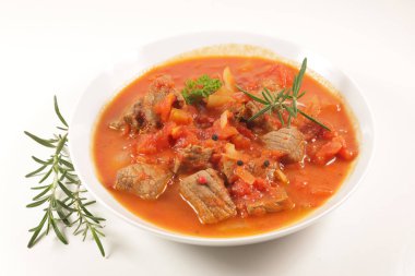 Domates soslu sığır güveci ve beyaz arka planda otlar.