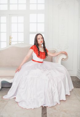 Kanepede oturan beyaz ve kırmızı ortaçağ elbiseli güzel kadın. 