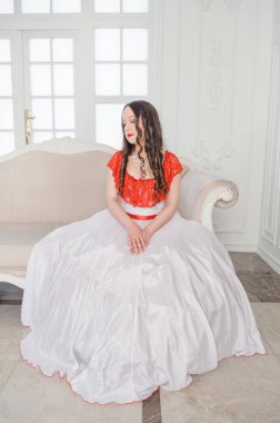 Kanepede oturan beyaz ve kırmızı ortaçağ elbiseli güzel kadın. 