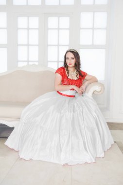 Kanepede oturan beyaz ve kırmızı ortaçağ elbiseli güzel kadın. 